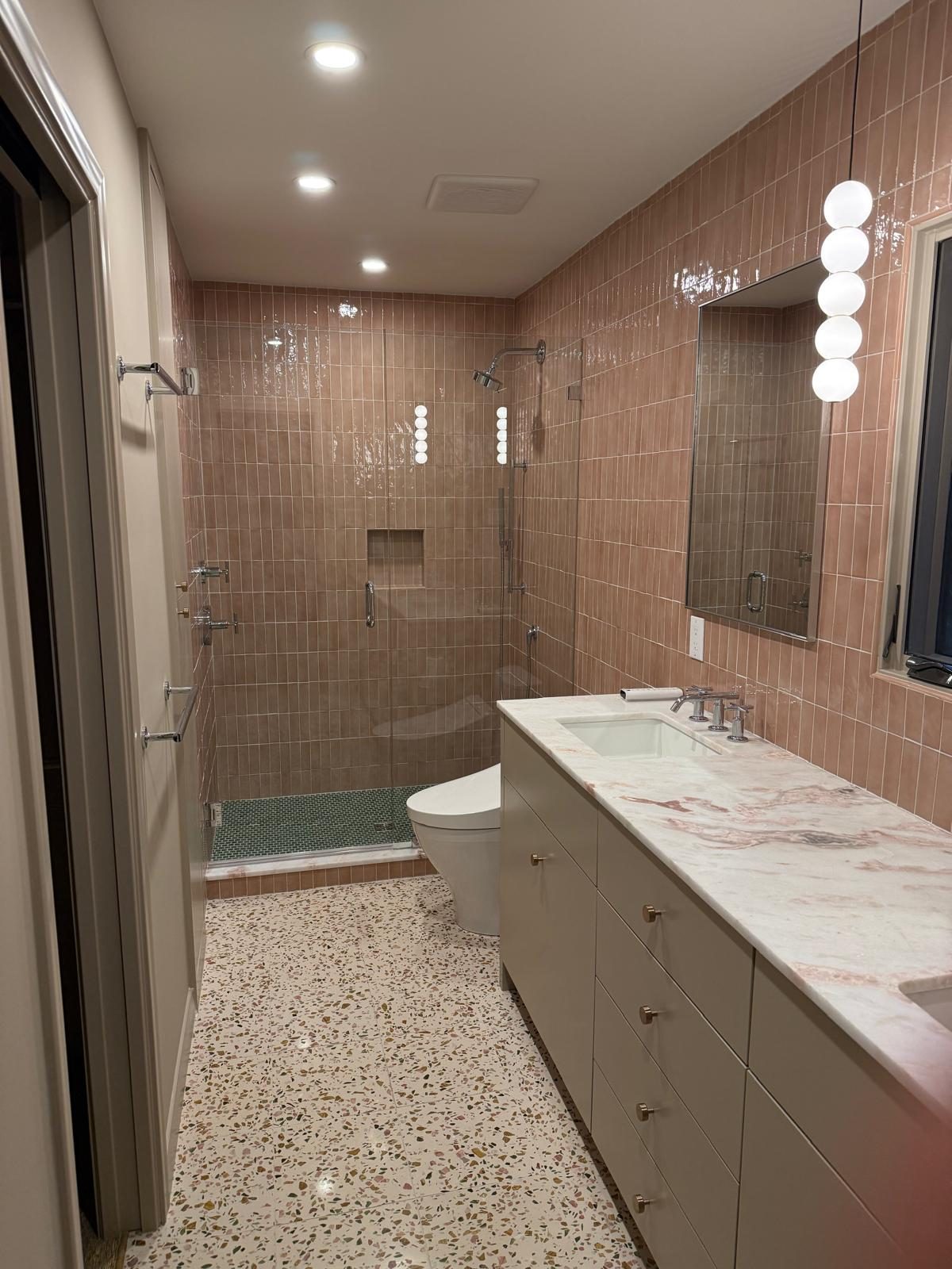 Glass walk-in shower framed by pink tile with a built-in niche