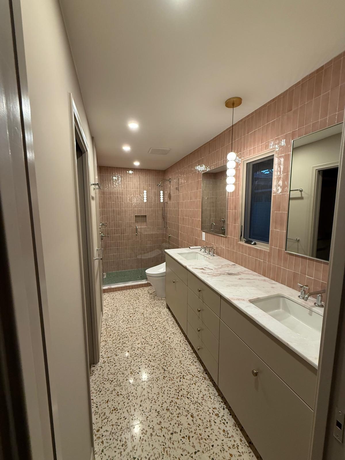 Wide view of a pink-tile bath with terrazzo floor and double vanity