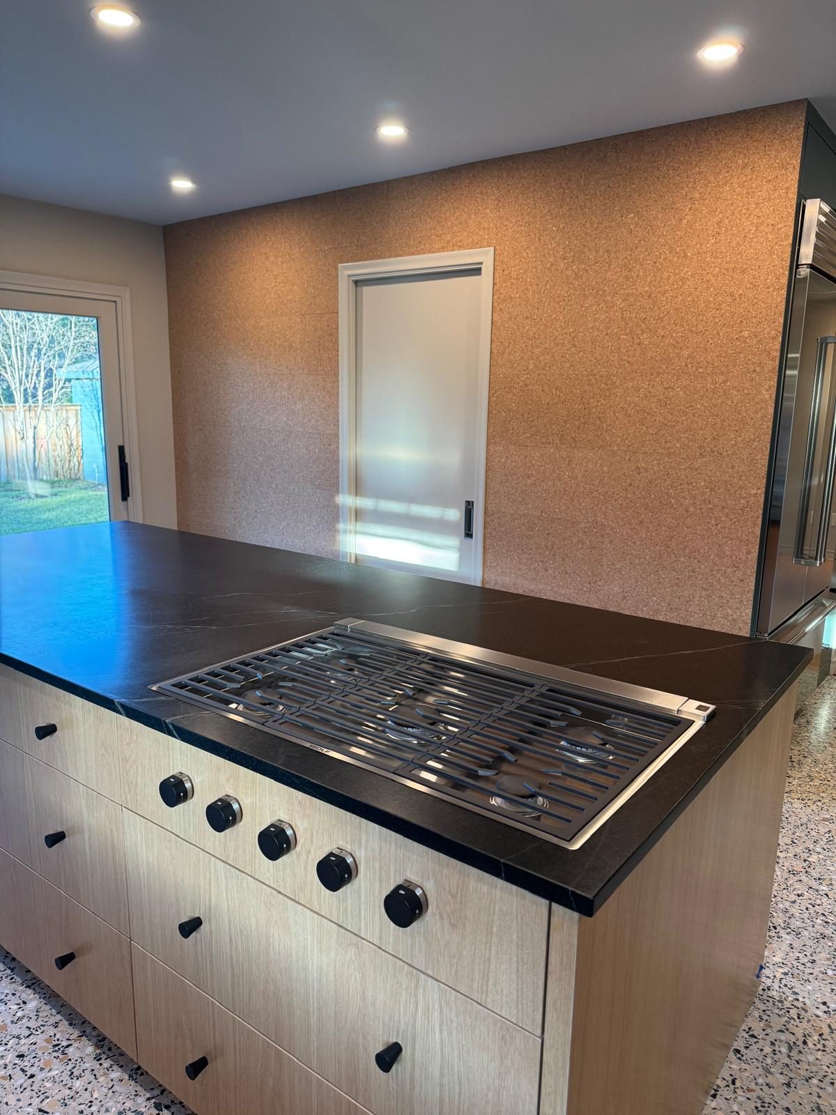Gas cooktop set into a black-stone island with light wood cabinets