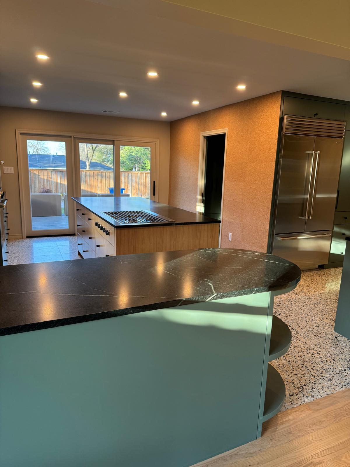 Kitchen island with black stone top opening onto a terrazzo floor and yard